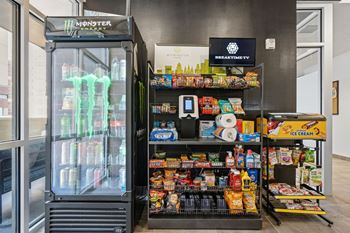 A monster branded cooler is next to a shelf with various snacks.